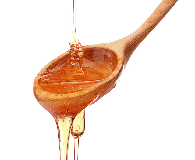 A wooden spoon with honey pouring out of it.